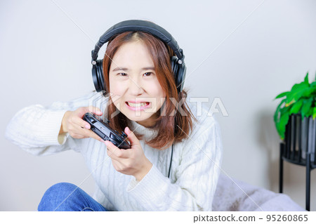 Japanese woman wearing headphones and enjoying video games indoors 95260865