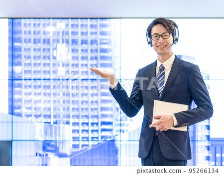 A businessman with a headset doing a recommended pose in front of a huge display A businessman with a headset doing a recommended pose in front of a huge display 95266134