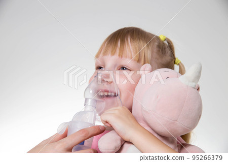 A little girl 5 years old in a pink T-shirt breathes into a nebulizer for lung disease. Treatment of bronchitis with inhalation, pharyngitis A little girl 5 years old in a pink T-shirt breathes into a nebulizer for lung disease. Treatment of bronchitis with inhalation, pharyngitis 95266379