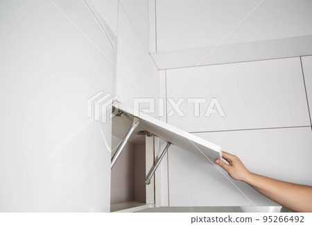 A furniture assembly worker holds a retractable gas spring to open and support a cabinet door. Modern furniture fittings, close-up 95266492