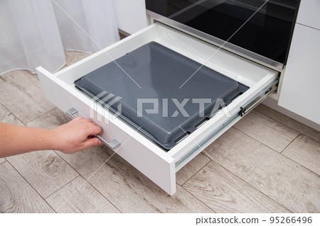 A man pulls out a drawer with baking sheets in the kitchen. A special compartment in the modern kitchen for storing baking sheets and pans, close-up 95266496