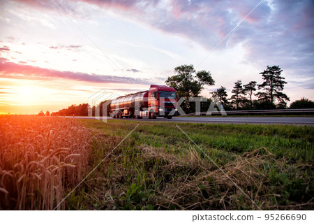A modern truck with a semi-trailer tanker transports dangerous goods against the backdrop of a sunset in summer. Liquid cargo transportation. Copy space for text A modern truck with a semi-trailer tanker transports dangerous goods against the backdrop of a sunset in summer. Liquid cargo transportation. Copy space for text 95266690