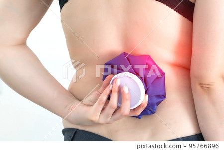 Girl holding a medical ice bag on the back of the spine. Concept for pain relief from muscle spasms and bruising pain. Therapeutics 95266896