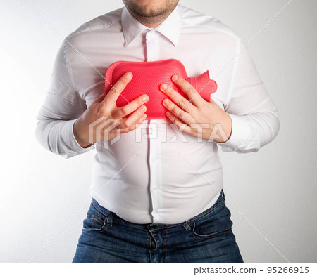 A man in a white shirt holds a red heating pad with hot water on his chest. Treatment of inflammation of the lungs and bronchitis by heating. Thermotherapy, close-up A man in a white shirt holds a red heating pad with hot water on his chest. Treatment of inflammation of the lungs and bronchitis by heating. Thermotherapy, close-up 95266915