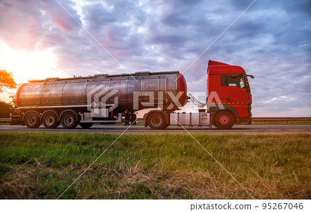A modern truck with a semi-trailer tanker transports dangerous goods against the backdrop of a sunset in summer. Liquid cargo transportation. Copy space for text, sanctions 95267046