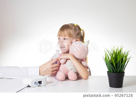 Beautiful little girl breathing into an inhaler for asthma and pneumonia at home. Treatment of diseases of the upper respiratory tract in children. Copy space for text Beautiful little girl breathing into an inhaler for asthma and pneumonia at home. Treatment of diseases of the upper respiratory tract in children. Copy space for text 95267128