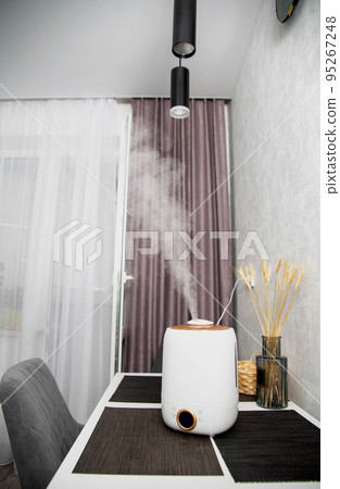 A modern humidifier sits on a table in a kitchen room. Humidification in the room, comfortable humidity and temperature 95267248
