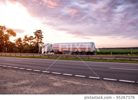 A truck with a semi-trailer tanker transports dangerous goods against the backdrop of a sunny sunset and the sky in the clouds. Transportation of fluid and liquid cargo in trucking industry, sanctions A truck with a semi-trailer tanker transports dangerous goods against the backdrop of a sunny sunset and the sky in the clouds. Transportation of fluid and liquid cargo in trucking industry, sanctions 95267376