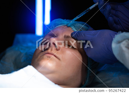 Doctor cosmetologist makes beauty injections to smooth forehead wrinkles. 95267422