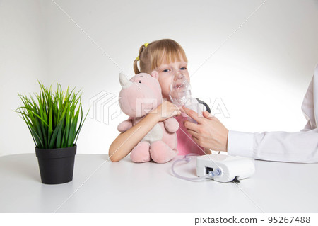 A 5-year-old caucasian girl is breathing into an inhaler at home. Treatment of cough and lung diseases in children, dilution of phlegm in the bronchi. 95267488
