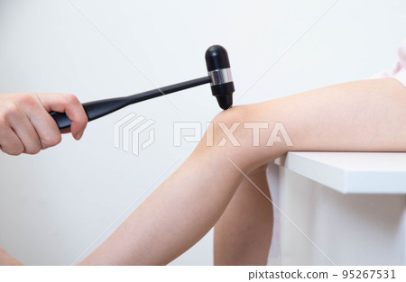 Hand of a neuropathologist doctor with a neurological hammer checks the reflex on the knee joint of a child, close-up 95267531