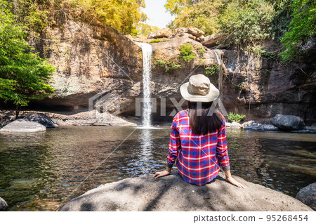 Freedom traveler woman alone sitting waterfall front on stone with bag and hat and a beautiful nature. Travel concept Freedom traveler woman alone sitting waterfall front on stone with bag and hat and a beautiful nature. Travel concept 95268454