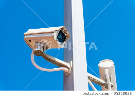 Digital surveillance camera is mounted on a pole with the blue sky in the background. 95268928