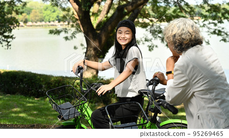 Senior grandmother and granddaughter walking with bicycle at park and talking to each other. Family time, old elderly concept 95269465