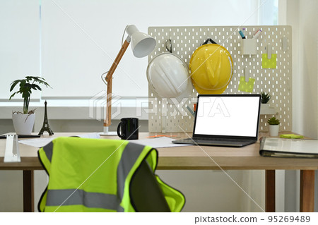 Architect working desk with laptop computer, hardhat, reflective jacket and stationery Architect working desk with laptop computer, hardhat, reflective jacket and stationery 95269489