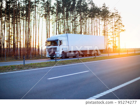 A modern truck with a refrigerated semi-trailer transports goods against the backdrop of a forest and an evening sunset in summer. the trucking industry. turnover. 95274277