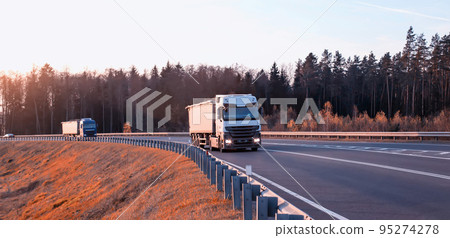 Trucks on the road with special trailers for the transport of bulk cargo of grain, crushed stone and sand against the background of the forest. Increased load capacity, industry 95274278
