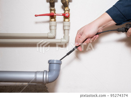 Cleaning the sewer drain pipe with a manual plumbing cable. Sewer blockage, close-up Cleaning the sewer drain pipe with a manual plumbing cable. Sewer blockage, close-up 95274374