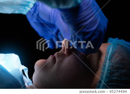 Doctor cosmetologist performs plastic surgery to correct the shape of the nostrils and nose of the patient's girl. Rhinoplasty, elimination of the siddle shape of the nose Doctor cosmetologist performs plastic surgery to correct the shape of the nostrils and nose of the patient's girl. Rhinoplasty, elimination of the siddle shape of the nose 95274494