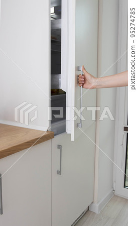 A man opens the door of a built-in refrigerator in the kitchen. Modern refrigerator placement technologies, renovation 95274785