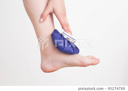 A girl applies a medical blue ice pack to the ankle joint to relieve pain and relieve swelling. Treatment of sports injuries and arthrosis of the leg joint 95274789