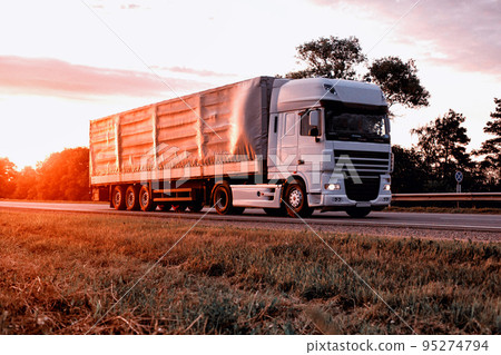 A truck with a tilt semi-trailer transports cargo against the backdrop of a sunset in the summer. Sharing economy concept in freight logistics. Modernization of logistics companies 95274794