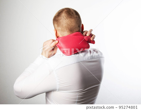 A man in a white shirt holds a medical heating pad with hot water on his cervical spine. Treatment of stiff neck muscles with heat, heat therapy A man in a white shirt holds a medical heating pad with hot water on his cervical spine. Treatment of stiff neck muscles with heat, heat therapy 95274801