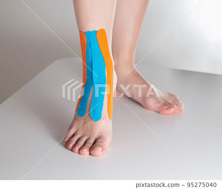 Fixation of the ankle joint on a woman's leg with a kinesiological tape, close-up. Alternative medicine 95275040