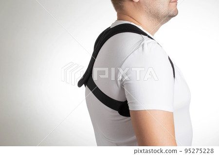 A man in a white T-shirt with a black posture corrector on a white background. Back pain and problem correction concept, treatment A man in a white T-shirt with a black posture corrector on a white background. Back pain and problem correction concept, treatment 95275228