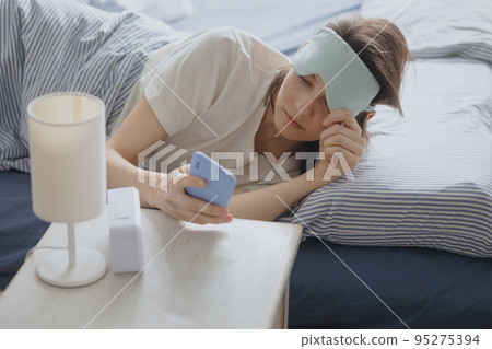 woman in bed with a sleep mask wakes up and talks on the phone. an unexpected call on a smartphone early in the morning or at night woman in bed with a sleep mask wakes up and talks on the phone. an unexpected call on a smartphone early in the morning or at night 95275394