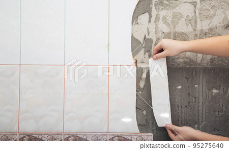 A man dismantles old tiles from the wall in the kitchen. Repair in the apartment, close-up A man dismantles old tiles from the wall in the kitchen. Repair in the apartment, close-up 95275640