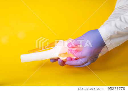Doctor's hands gluing a medical plaster on a model of a sore knee joint, yellow background. Knee pain concept, synovitis and bursitis treatment, chlamydia. Copy space for text 95275778