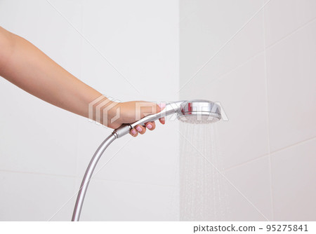Girl in hand holds a shower in the bathroom against the background of a white wall, close-up Girl in hand holds a shower in the bathroom against the background of a white wall, close-up 95275841