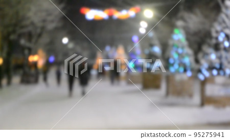 Blurred background. City street during snowfall at winter night. Beautiful illumination and decoration on street. New Year Christmas holidays celebration. Lanterns garlands on trees. 95275941