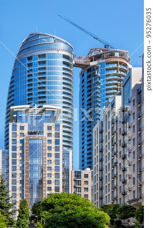 Glass facade of a modern multi-storey residential building under construction against a blue background of the summer sky. 95276035