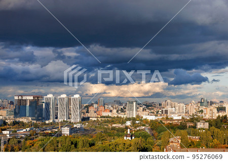 Thunderclouds over the city illuminated by the rays of the evening sun. Beautiful cityscape from a bird's eye view. Thunderclouds over the city illuminated by the rays of the evening sun. Beautiful cityscape from a bird's eye view. 95276069