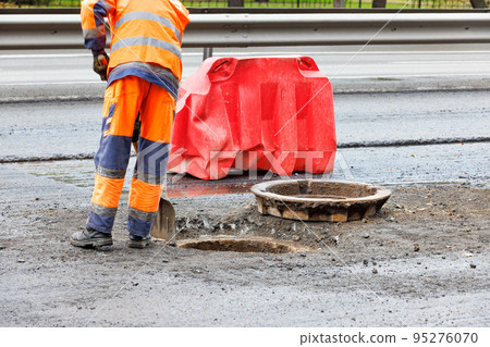 A road worker cleans the mouth of a sewer manhole on the carriageway. A road worker cleans the mouth of a sewer manhole on the carriageway. 95276070