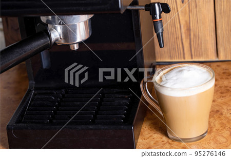 Making coffee with cappuccino milk in a cappuccino machine with a manual cappuccino maker on the background of a wooden table top. Close-up Making coffee with cappuccino milk in a cappuccino machine with a manual cappuccino maker on the background of a wooden table top. Close-up 95276146