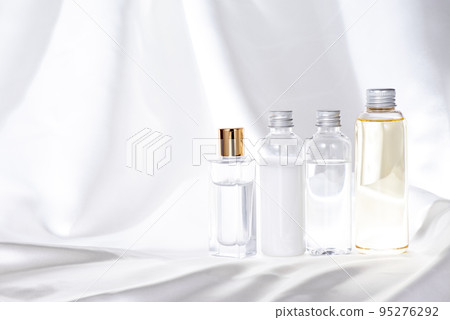 白色緞布上排列的四個玻璃和塑料化妝品瓶 95276292