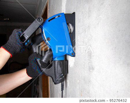 A worker in gloves works with an electric tool with a wall chaser on a reinforced concrete wall. Copy space for text 95276432