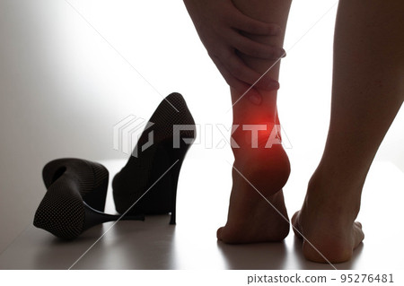 The girl holds on to the inflamed ankle joint, high heels are next to her. Concept of leg joint pain due to uncomfortable shoes 95276481