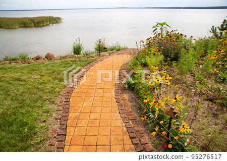 Tile path in the country house around lawns and flower beds which leads to the lake. Landscape design, background 95276517
