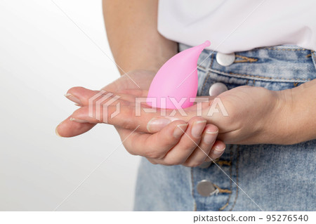The girl holds a pink menstrual cup in her hands to collect the discharge during menstruation. New in Gynecology, Replacement of Feminine Sanitary Pads and Tampons 95276540