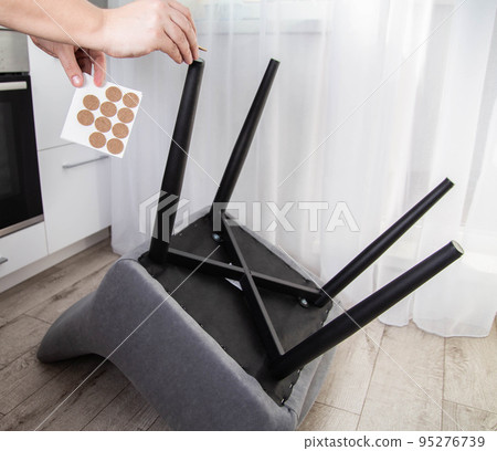 A man glues protective pads on the legs of a chair. Protection against floor scratches and noise A man glues protective pads on the legs of a chair. Protection against floor scratches and noise 95276739