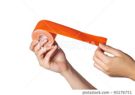 The girl holds in her hands on a white background a kinesiological tape of orange color, isolate. Taping muscles and joints, close-up The girl holds in her hands on a white background a kinesiological tape of orange color, isolate. Taping muscles and joints, close-up 95276751