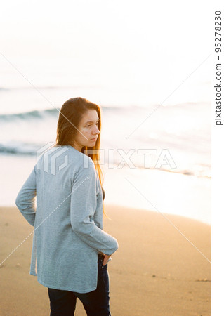 Girl in a sweater with her hands in her pockets stands on the seashore and looks away 95278230
