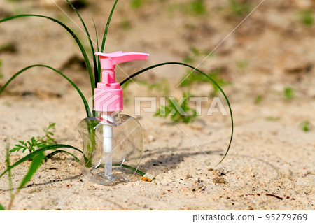 Pink transparent spray bottle for antiseptic and perfume on sand with greenery 95279769