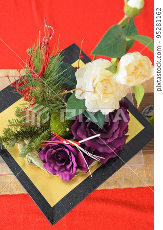 紅色桌布和新年裝飾品。白色山茶花和紫葉牡丹、松樹和紅色漿果。 紅色桌布和新年裝飾品。白色山茶花和紫葉牡丹、松樹和紅色漿果。 95281162