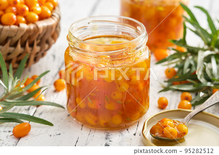 Jar of healthy sea buckthorn jam. Basket of ripe sea buckthorn berries on background. A spoonful of sea buckthorn jam in the foreground. Jar of healthy sea buckthorn jam. Basket of ripe sea buckthorn berries on background. A spoonful of sea buckthorn jam in the foreground. 95282512