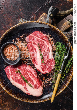 Chuck eye Roll beef steaks, raw meat on a plate with thyme and herbs. Dark background. Top view 95282924